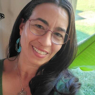 Head shot of Lynda Hamilton looking at camera with tilted head, long brown hair, eyeglasses, and a smile.