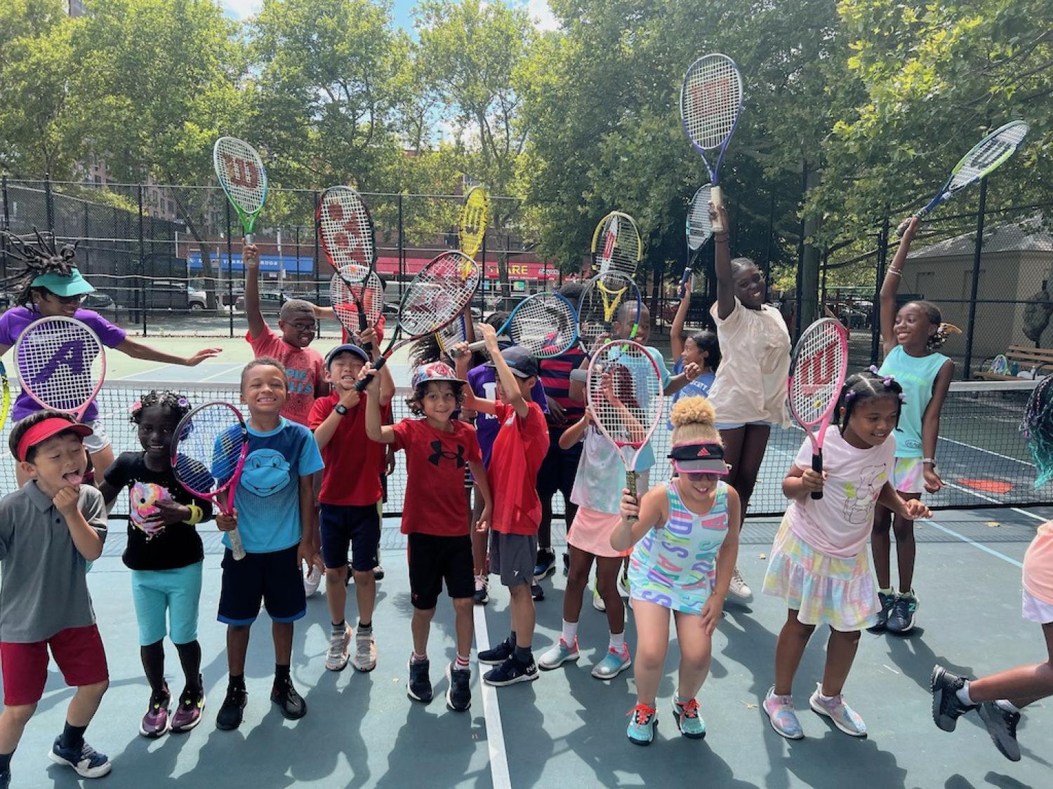 Large group of youth raising their tennis rackets on a sunny date at an outside tennis court