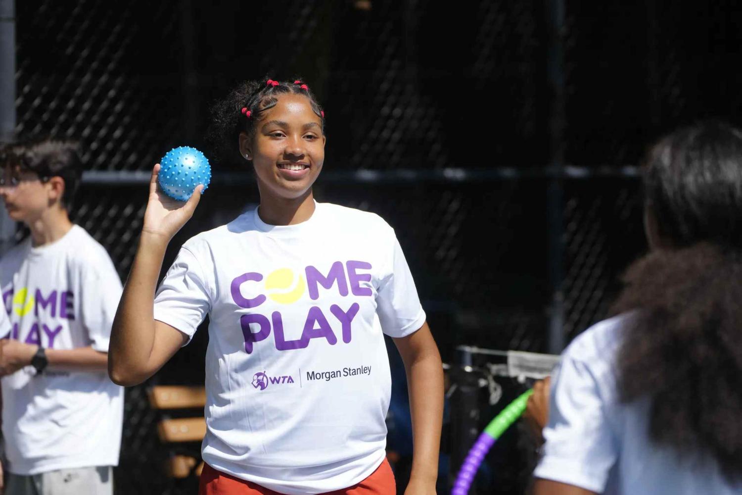 HJTEP female youth holding up blue ball at the Come Play Summer Tennis Clinic