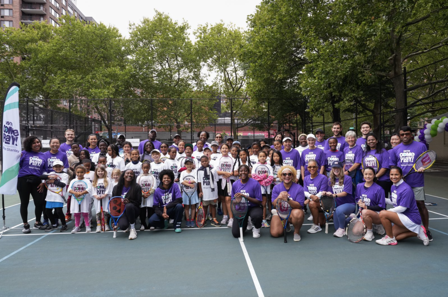 A large group of young athletes and coaches in a group photo on the tennis court.