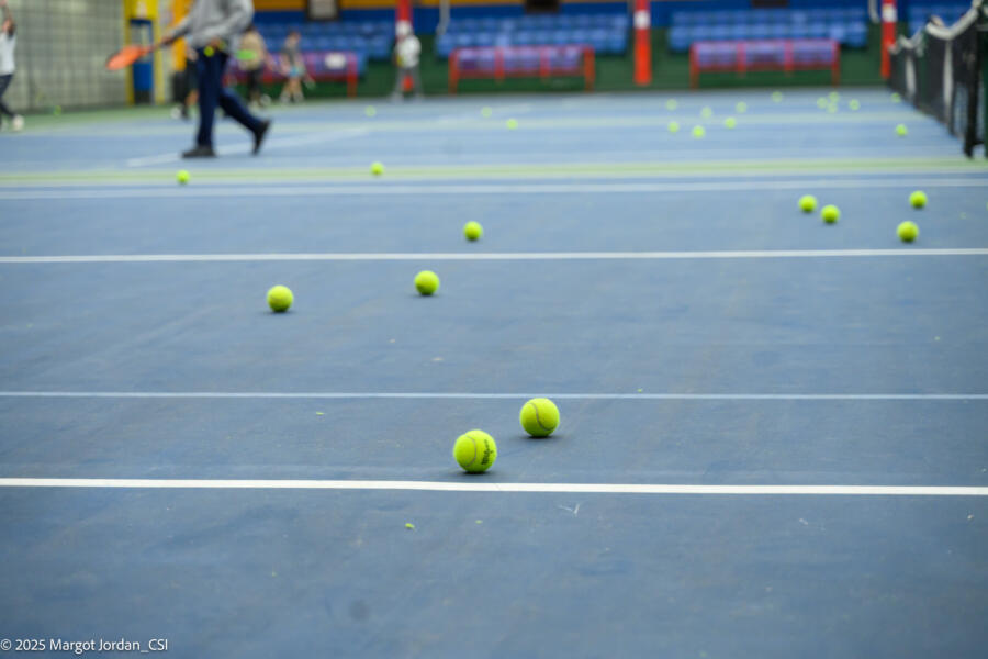 Tennis balls scattered across a blue court surface with white lines, showing the results of a practice session or lesson.