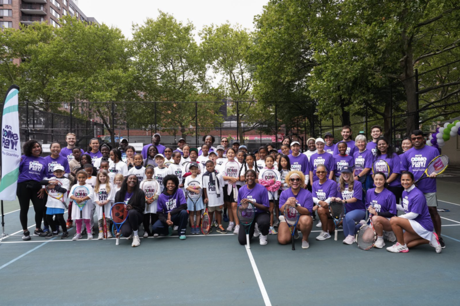 A large group of young athletes and coaches in a group photo on the tennis court.